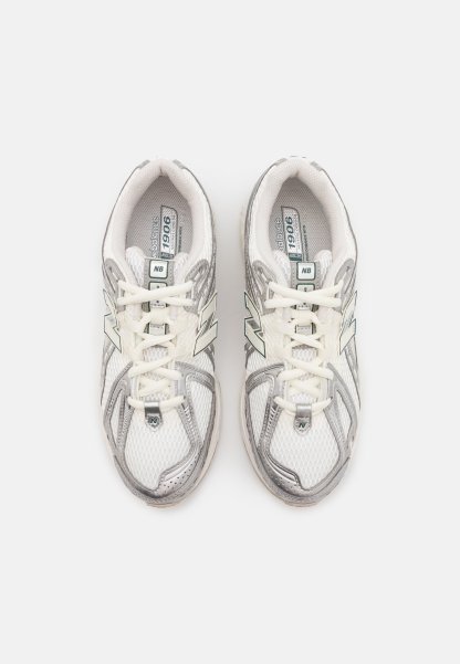 Zapatillas deportivas blancas de malla con detalles en plata. Las características incluyen cordones, una marca en la lengüeta y una suela acolchada. La parte superior tiene un diseño texturizado.