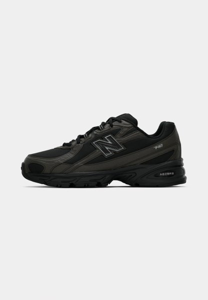 Zapatillas deportivas negras con un upper sintético texturizado, que cuentan con una suela acolchada y un prominente logo "N" en el lateral. El diseño incluye secciones de malla ligera.