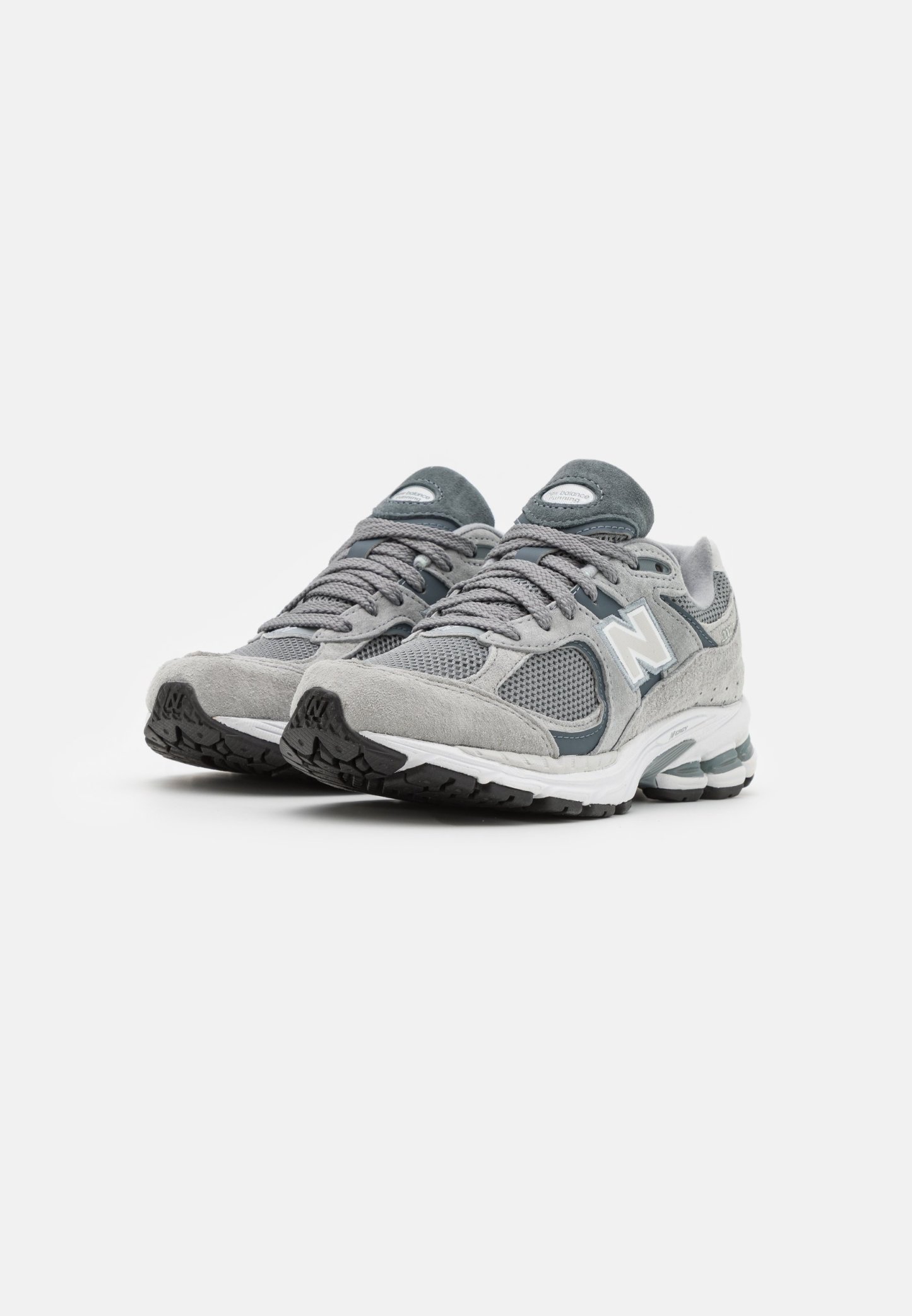 Zapatillas deportivas gris con parte superior de malla y ante, punta redondeada, media suela gruesa blanca y suela exterior negra texturizada. Detalles en gris más oscuro.