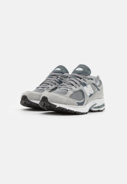 Zapatillas deportivas gris con parte superior de malla y ante, punta redondeada, media suela gruesa blanca y suela exterior negra texturizada. Detalles en gris más oscuro.
