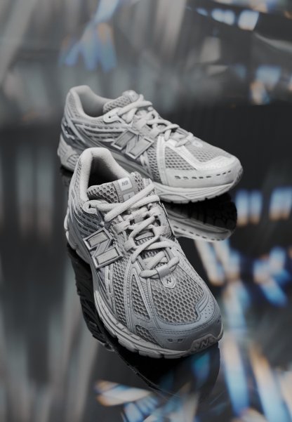 Zapatillas deportivas grises que presentan materiales de malla y sintéticos, puntera redondeada, suela acolchada, sistema de cordones y un destacado logo "N" en el costado.