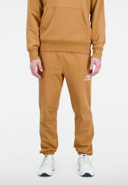 Pantalones de chándal color tostado con cintura y puños elásticos. Presentan un logo blanco de New Balance en el muslo izquierdo. El material parece suave y liso.