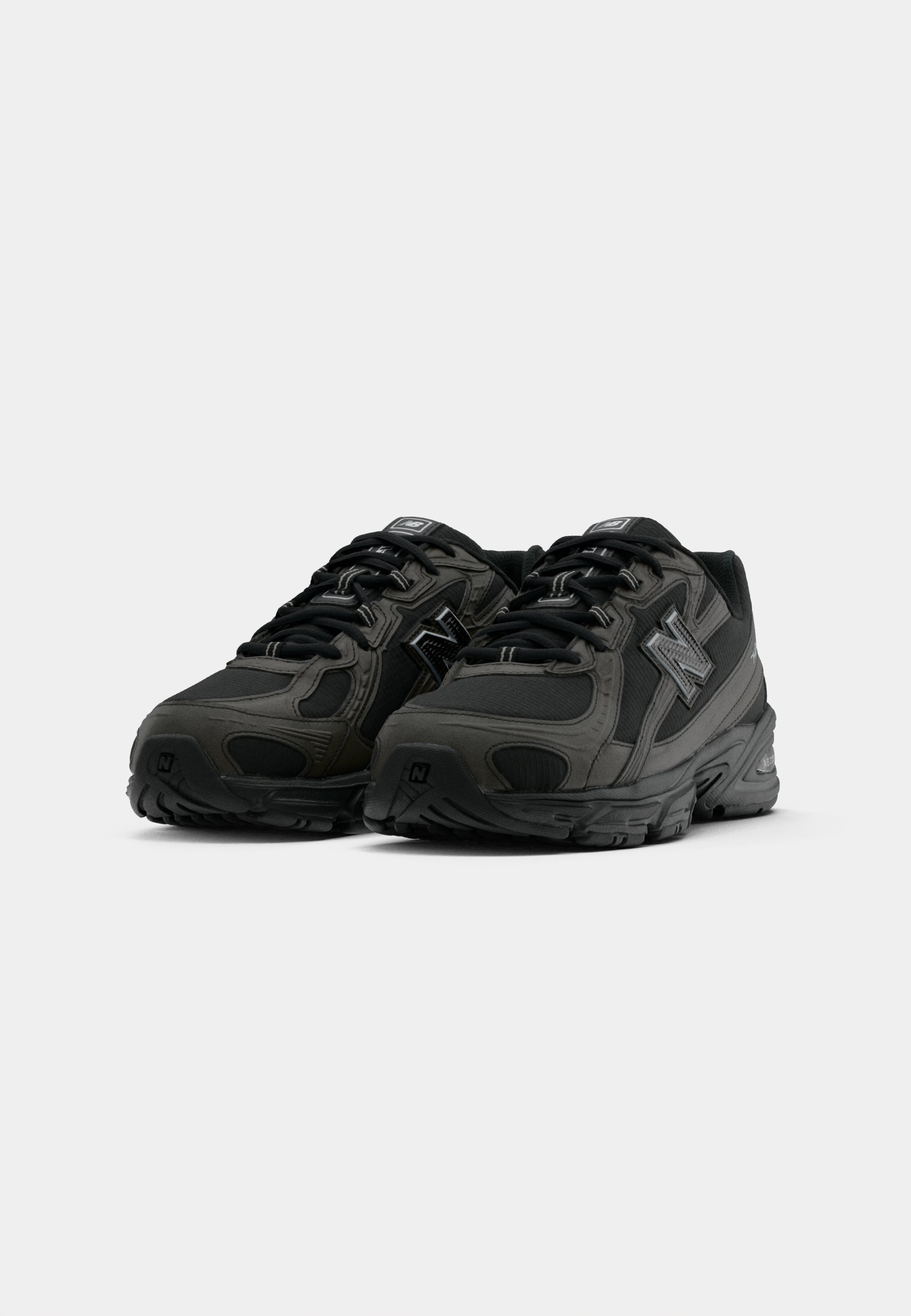 Par de zapatillas deportivas de New Balance en negro y gris oscuro con cordones, parte superior de malla y sintético, vista frontal en ángulo sobre fondo blanco.