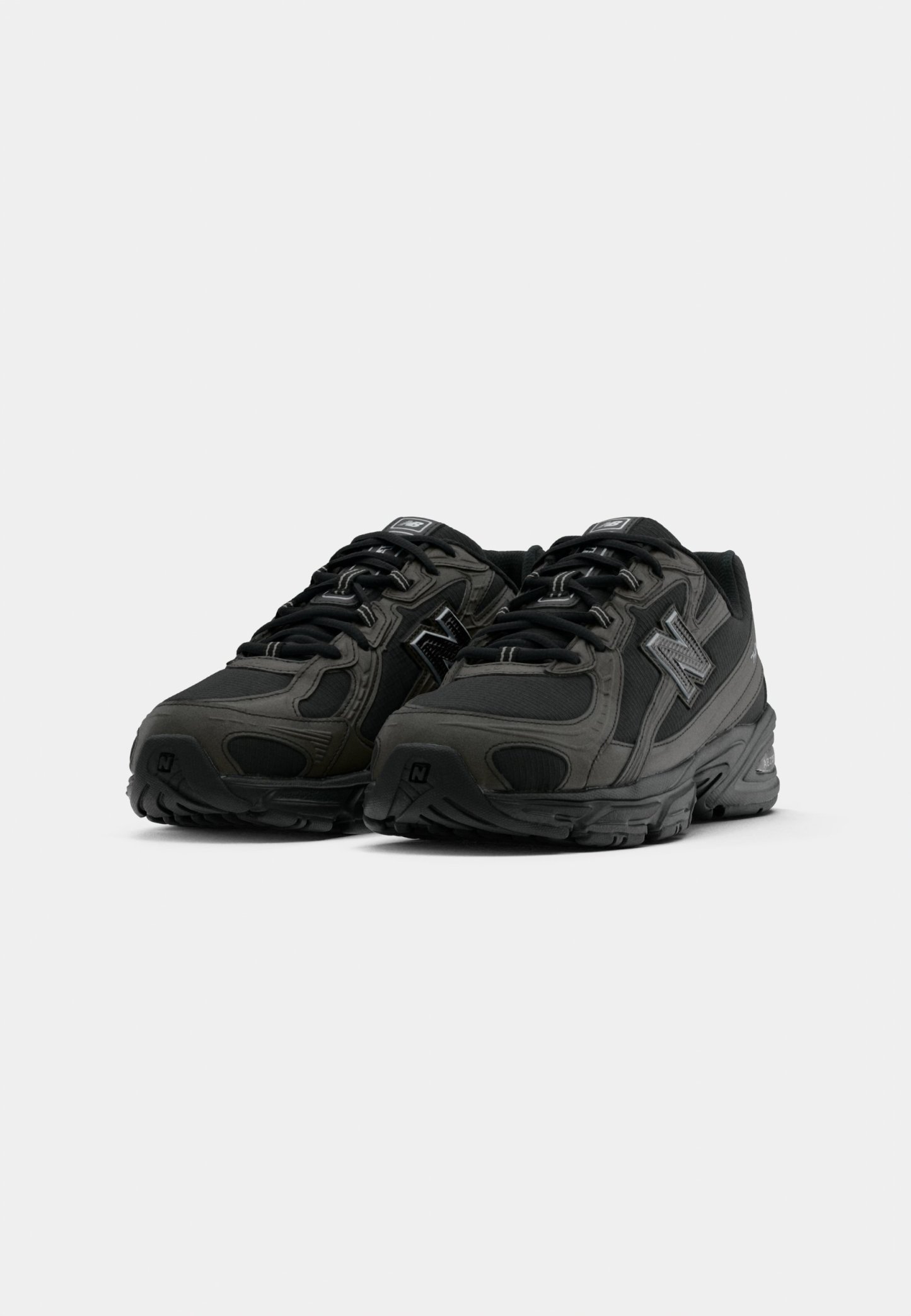 Par de zapatillas deportivas de New Balance en negro y gris oscuro con cordones, parte superior de malla y sintético, vista frontal en ángulo sobre fondo blanco.
