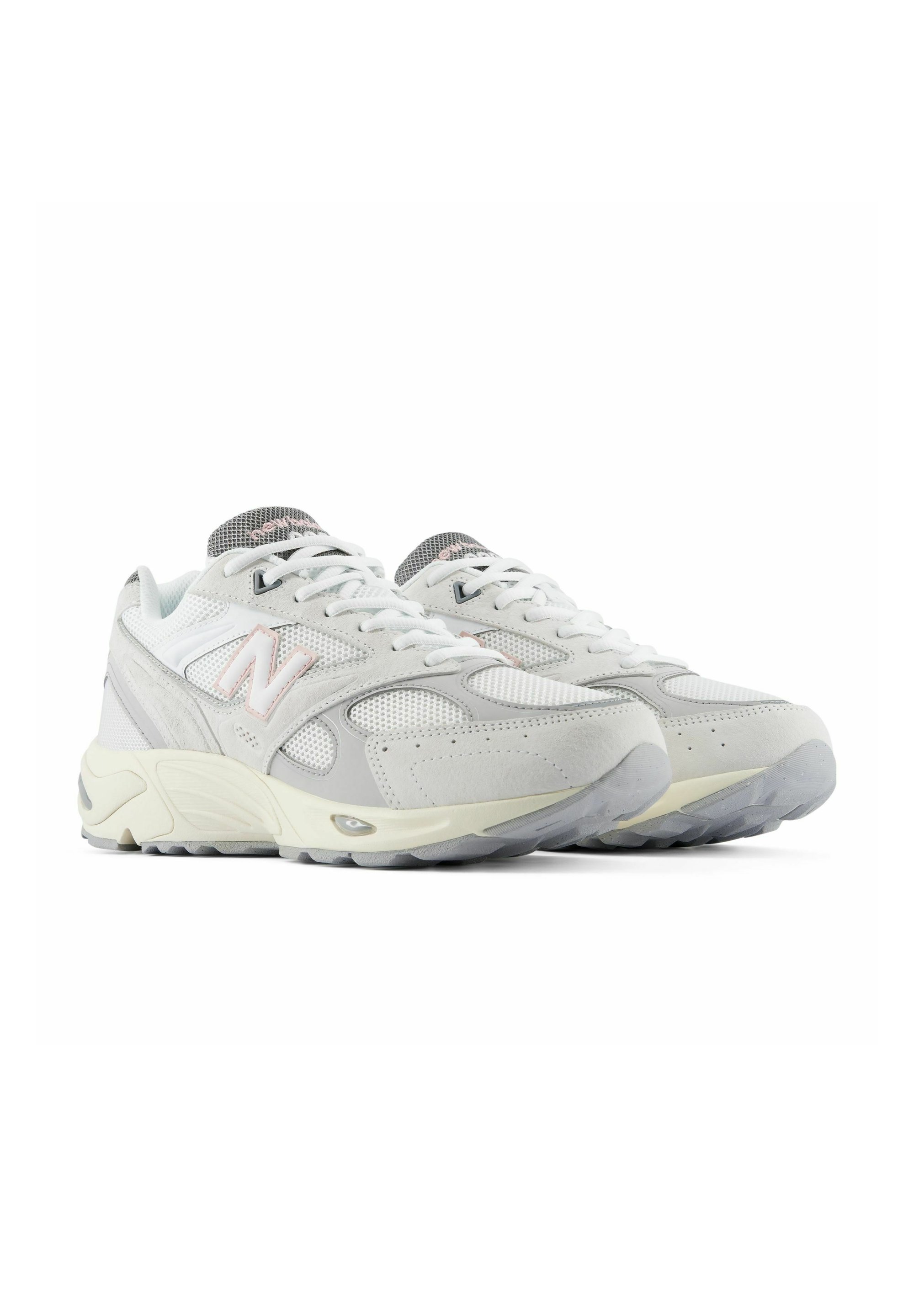 Par de zapatillas de running New Balance blancas y grises con detalles de malla y ante, acentos de logo en rosa claro y suelas gruesas de goma.