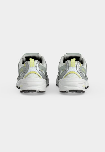 Par de zapatillas deportivas grises y blancas con detalles amarillos, mostradas desde atrás sobre un fondo claro y liso.