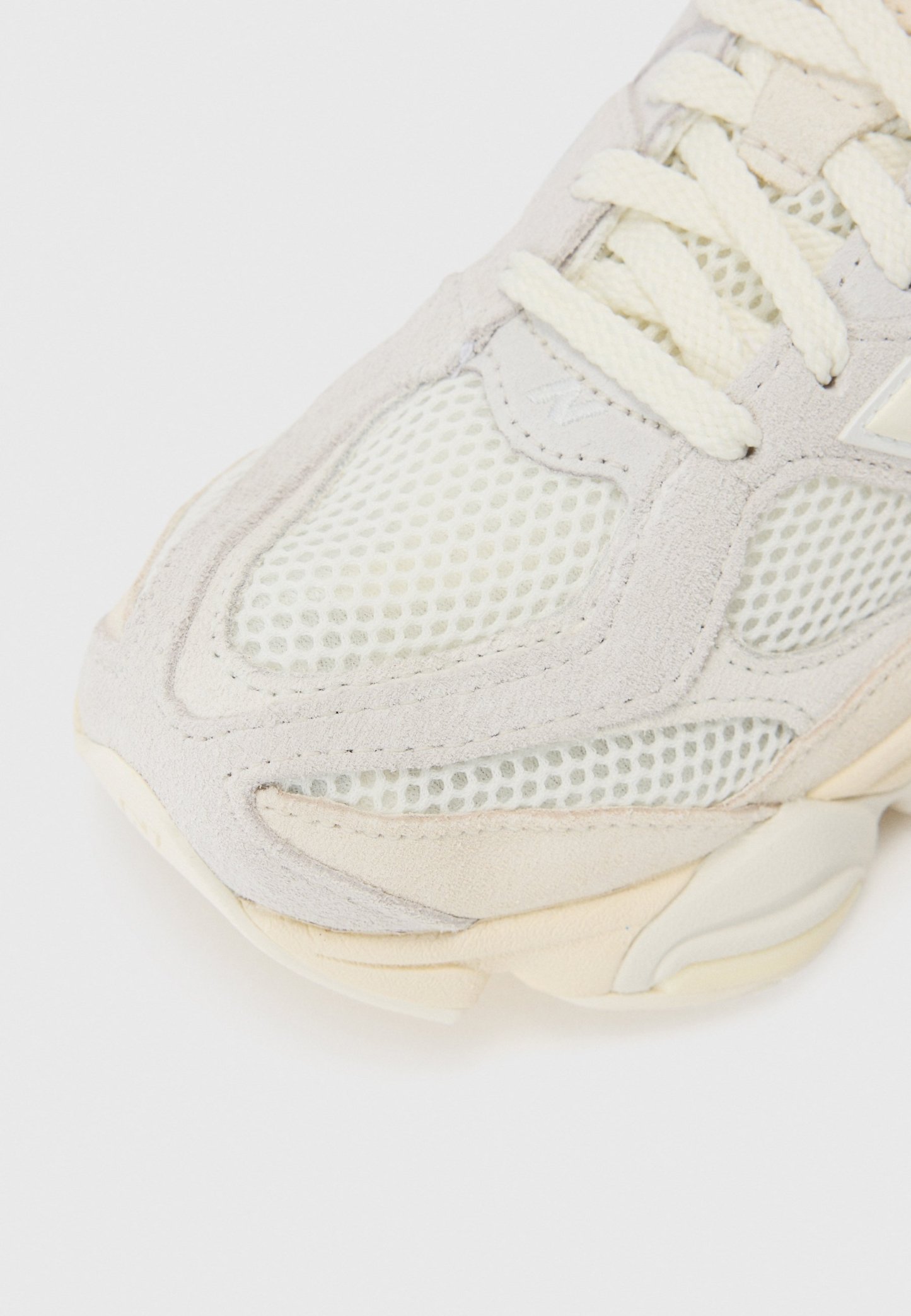 Zapatilla gris claro con paneles de malla y acentos de ante. Cuenta con una suela de goma texturizada y cordones beige, diseñada para comodidad y soporte.