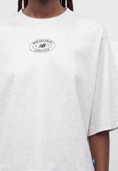 Primer plano de una persona que lleva una camiseta New Balance Athletics de color gris claro con un pequeño logo negro en el pecho y una etiqueta en el lateral.
