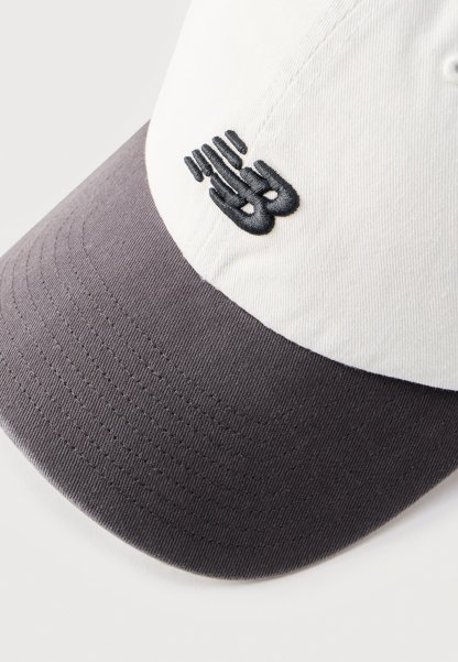 Gorra de béisbol con corona blanca y visera gris oscuro, con un pequeño logo abstracto negro bordado en el panel frontal.