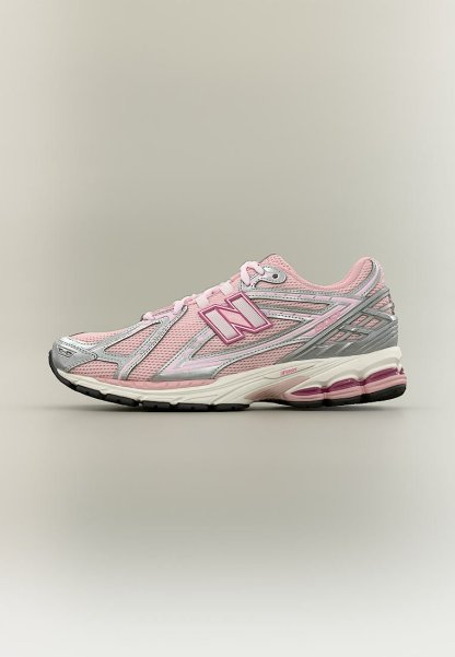 Zapatilla de running New Balance rosa claro con detalles en plata y blanco, parte superior de malla transpirable y suela acolchada con unidades de aire visibles.