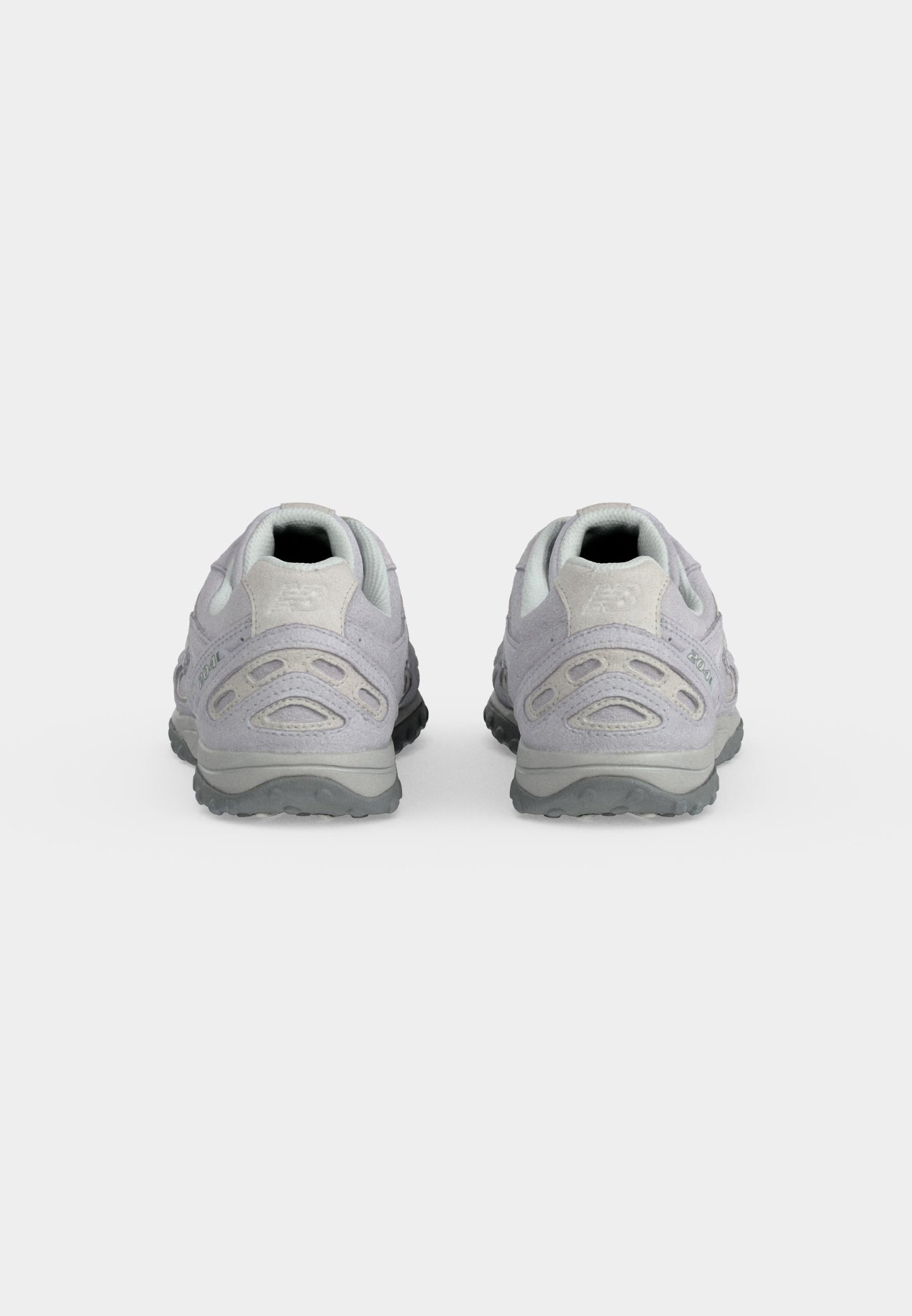 Par de zapatillas deportivas de color gris claro vistas desde los talones, con suelas texturizadas y detalles en ante sobre un fondo blanco.