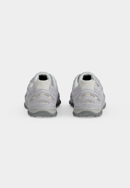 Par de zapatillas deportivas de color gris claro vistas desde los talones, con suelas texturizadas y detalles en ante sobre un fondo blanco.