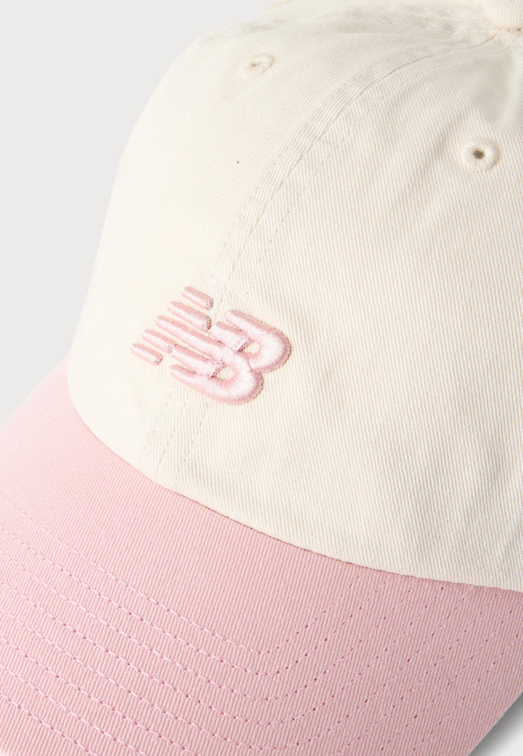 Gorra de béisbol con corona color crema y visera rosa que presenta un logo bordado en rosa en el panel frontal.