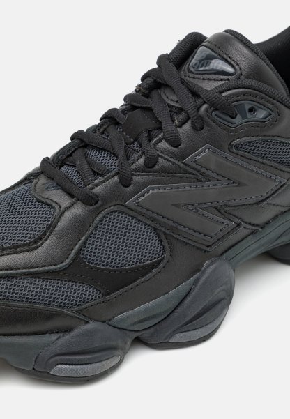 Zapatilla deportiva negra que presenta materiales de cuero sintético y malla, puntera redondeada, un sistema de cordones prominente y detalles en la suela texturizada.