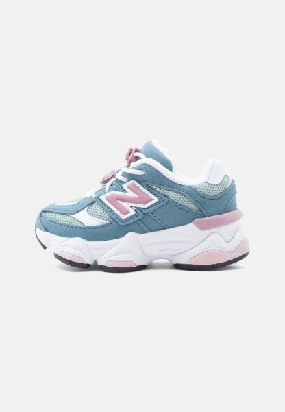 Zapatilla deportiva azul y blanca con detalles en rosa, paneles de malla y ante, suela blanca gruesa y cordones, mostrada de lado sobre un fondo liso.