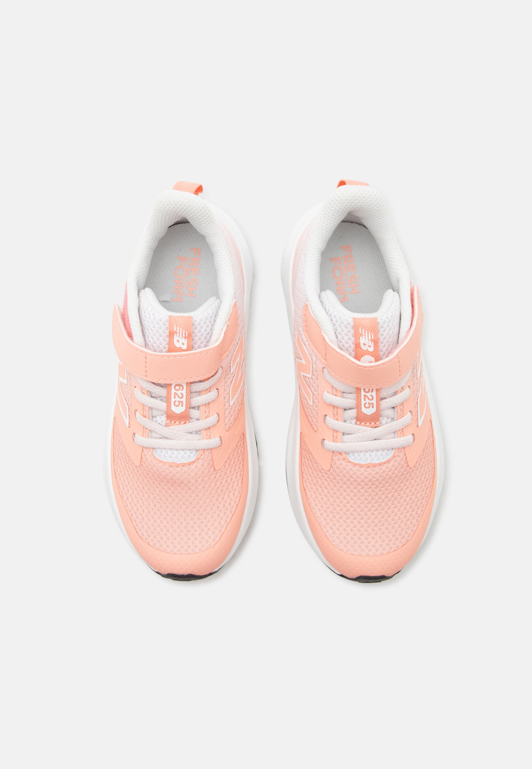 Par de zapatillas deportivas infantiles en color melocotón y blanco con tira de velcro y cordones, parte superior de malla, y suela acolchada blanca, vistas desde arriba.