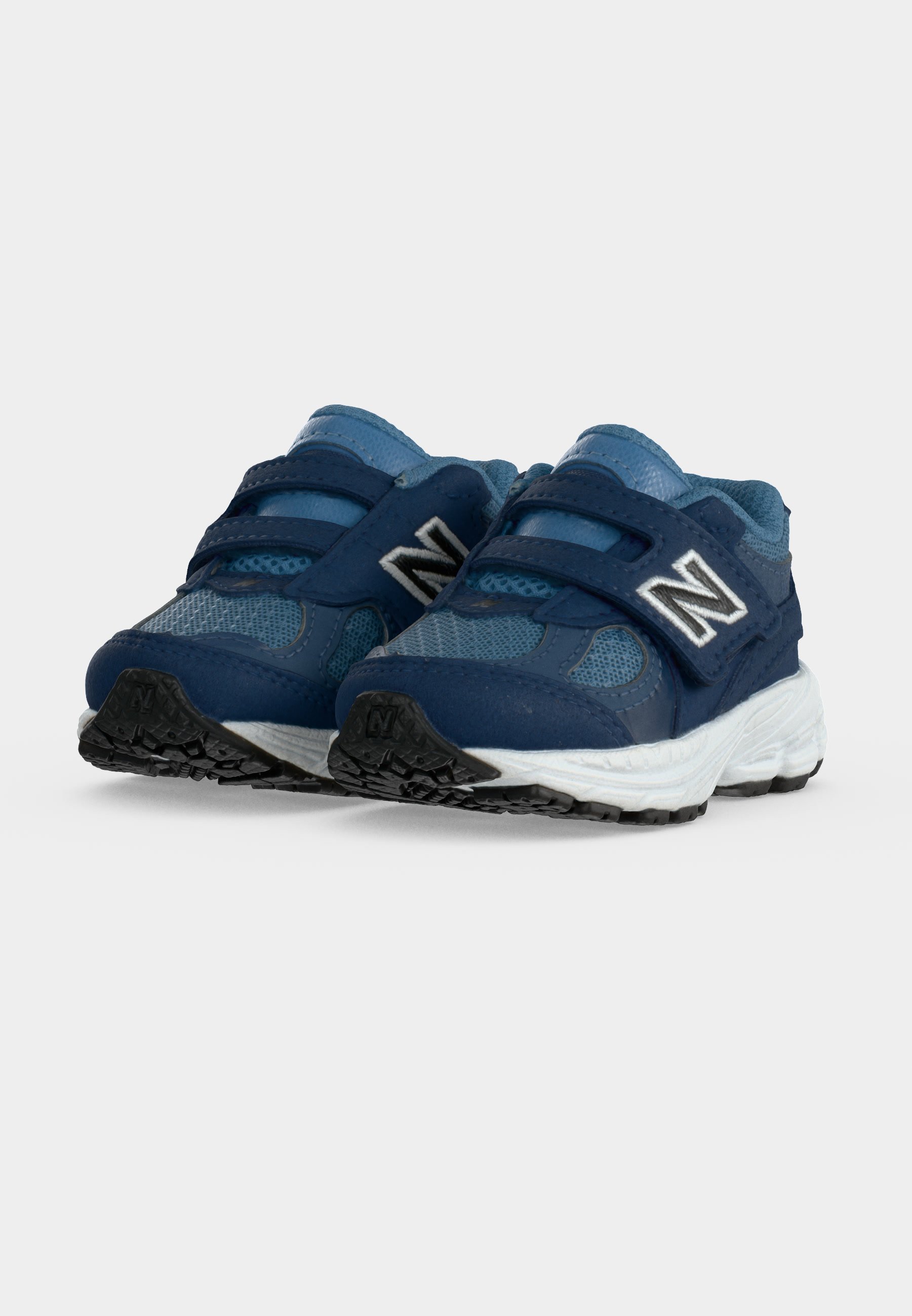 Par de zapatillas infantiles azules con tiras de velcro y suelas blancas sobre un fondo liso gris claro.