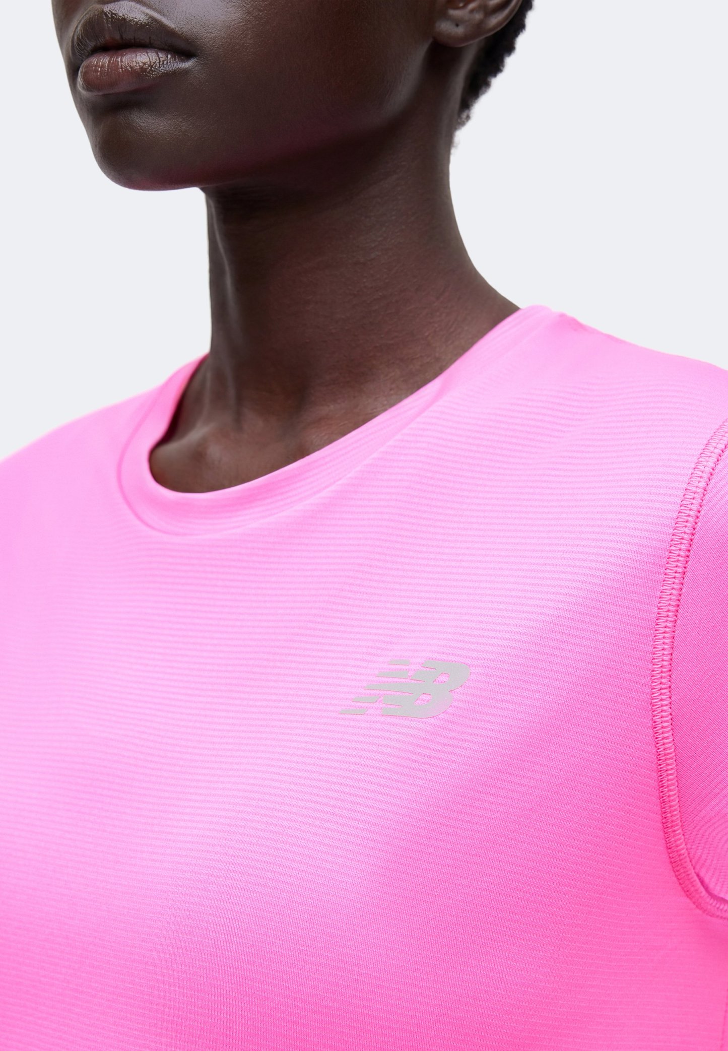 Primer plano de una persona con una camiseta deportiva New Balance de color rosa brillante con escote redondo y logo reflectante en el pecho.