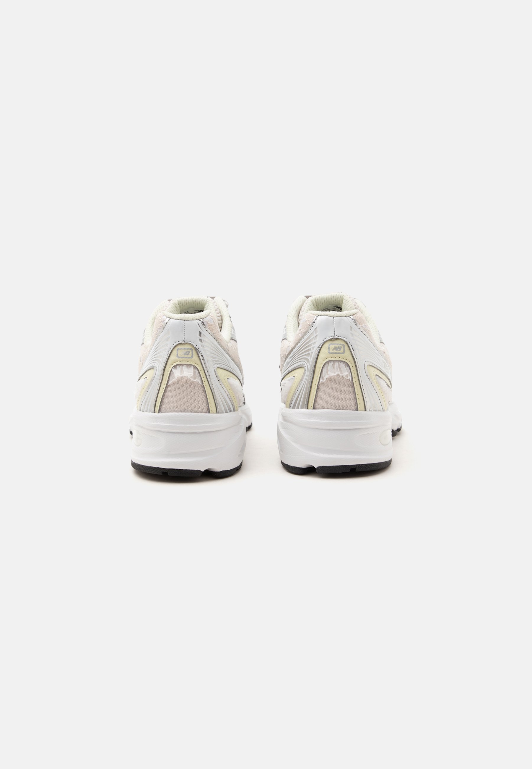 Par de zapatillas deportivas blancas con detalles beige vistas desde atrás sobre un fondo blanco liso.