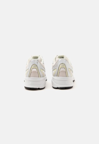 Par de zapatillas deportivas blancas con detalles beige vistas desde atrás sobre un fondo blanco liso.