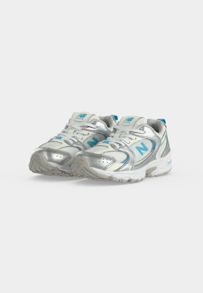 Par de zapatillas de correr New Balance plateadas y blancas con detalles en azul sobre fondo blanco.