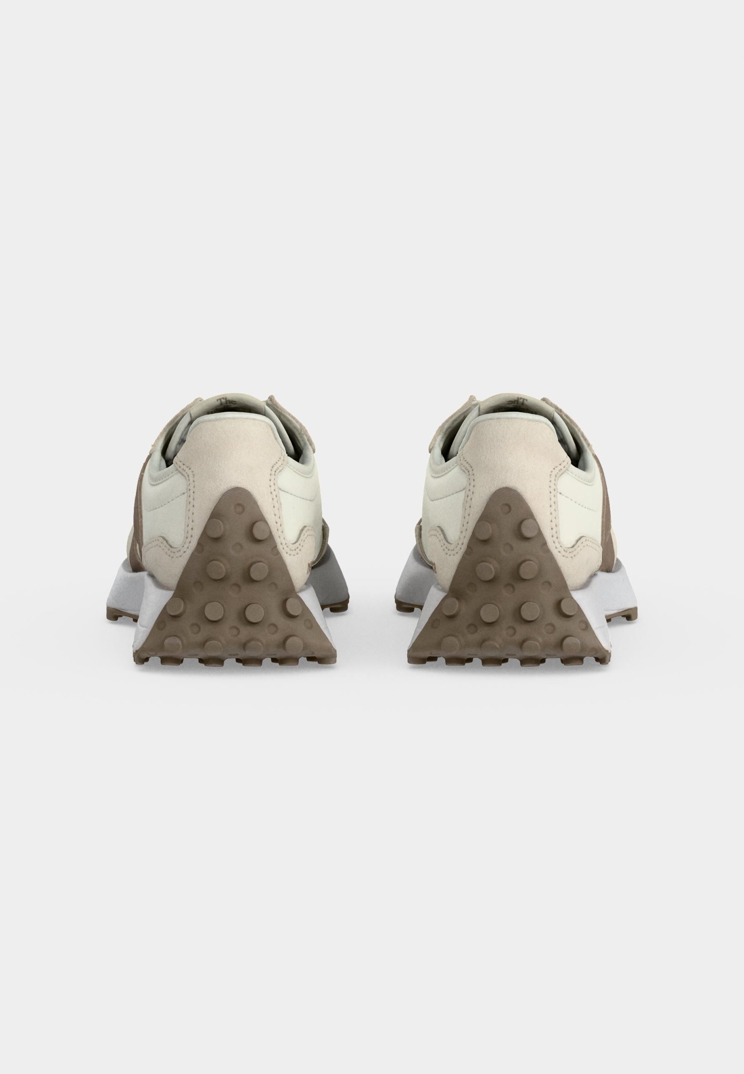 Par de zapatillas beige y blancas vistas desde atrás, con cubiertas de goma texturizadas en el talón en forma triangular con agarres circulares.