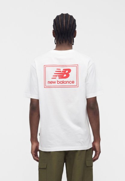 Persona con el cabello trenzado que lleva una camiseta blanca con el logo rojo "NB new balance" en la parte trasera y pantalones cargo verde oliva, de espaldas.