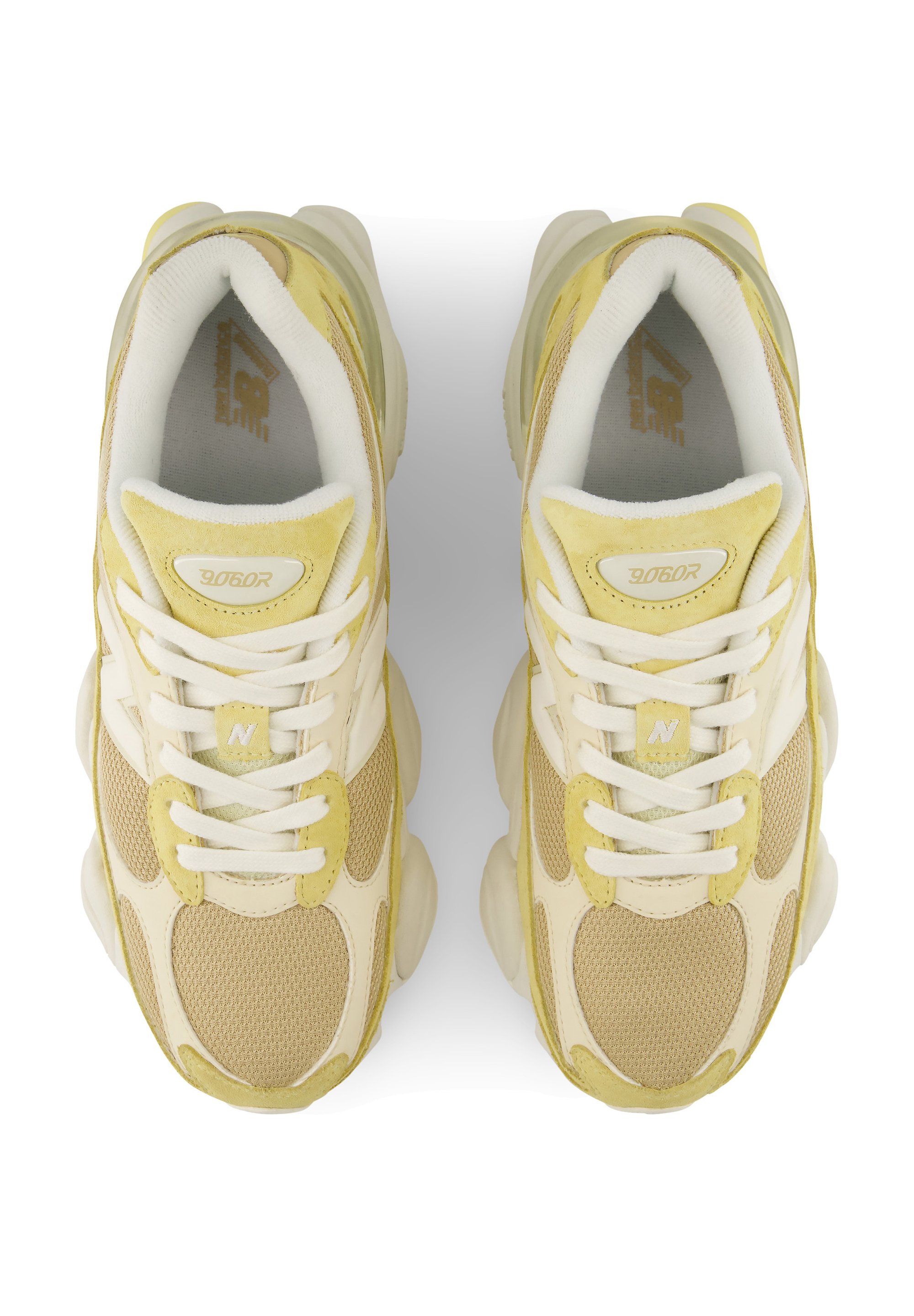 Par de zapatillas deportivas beige y amarillas con cordones blancos vistas desde arriba sobre un fondo blanco.