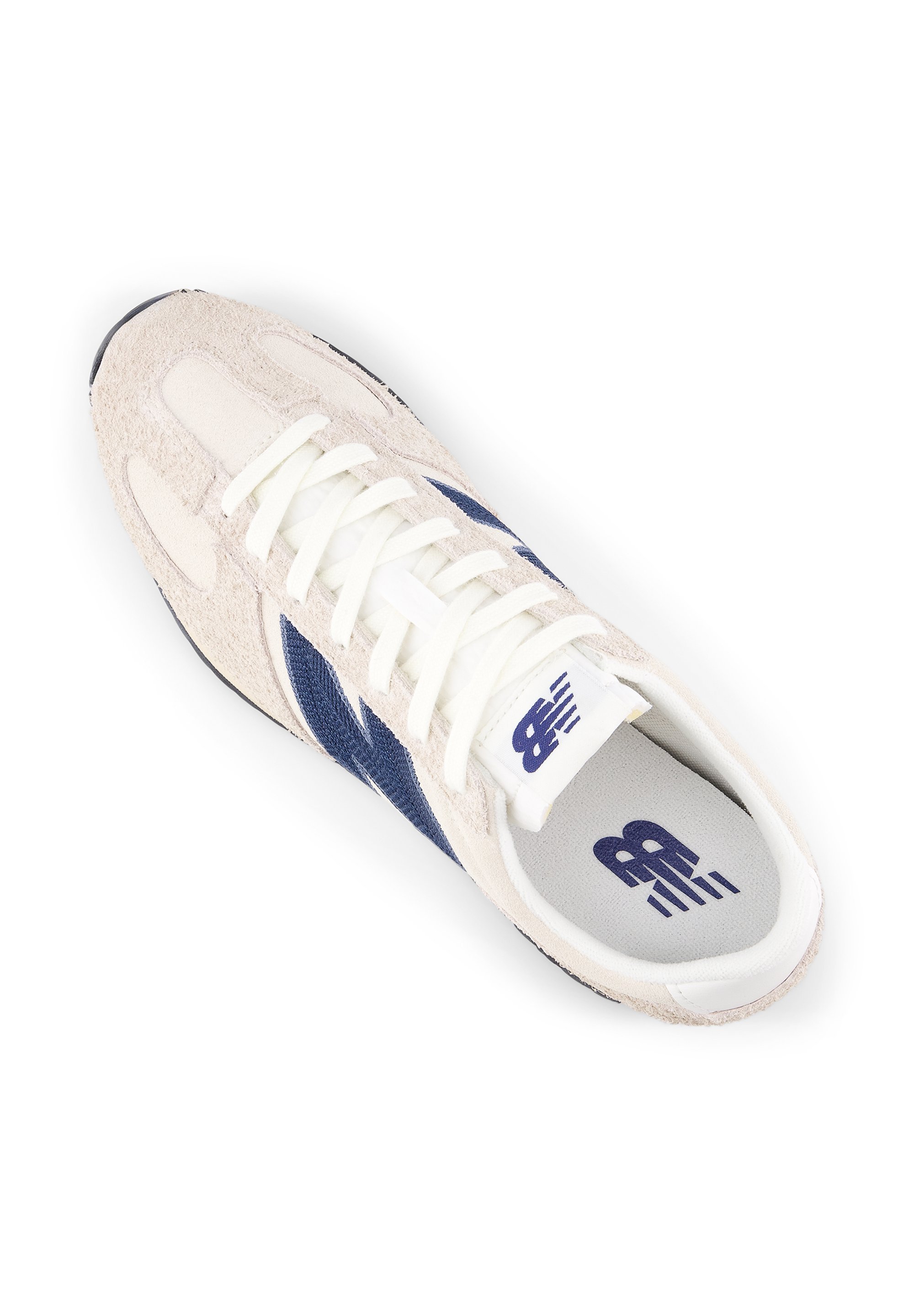 Zapatilla deportiva con materiales de ante crema y malla azul marino, cordones blancos, suela de goma texturizada y logo impreso en la lengüeta.