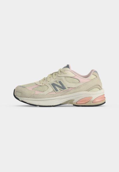 Zapatilla de running New Balance beige y rosa pastel con detalles de malla y ante, logo en el lateral y suela acolchada con acentos rosas.