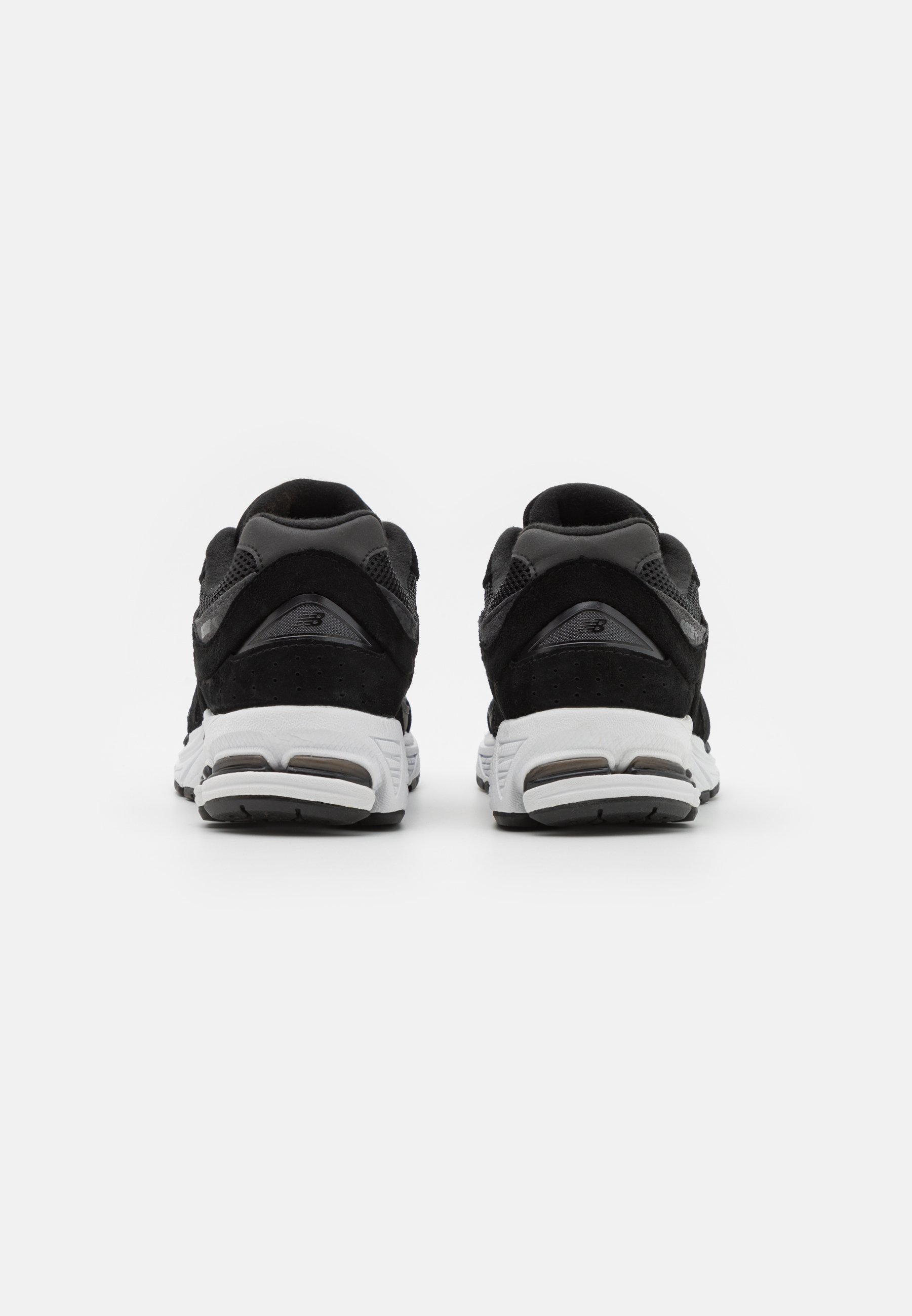 Zapatillas deportivas negras con una mezcla de materiales de ante y malla; cuentan con una suela blanca, forma redondeada y un branding minimalista en el talón.