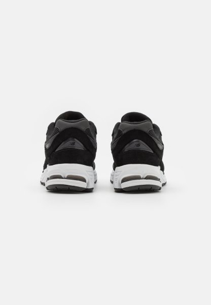 Zapatillas deportivas negras con una mezcla de materiales de ante y malla; cuentan con una suela blanca, forma redondeada y un branding minimalista en el talón.