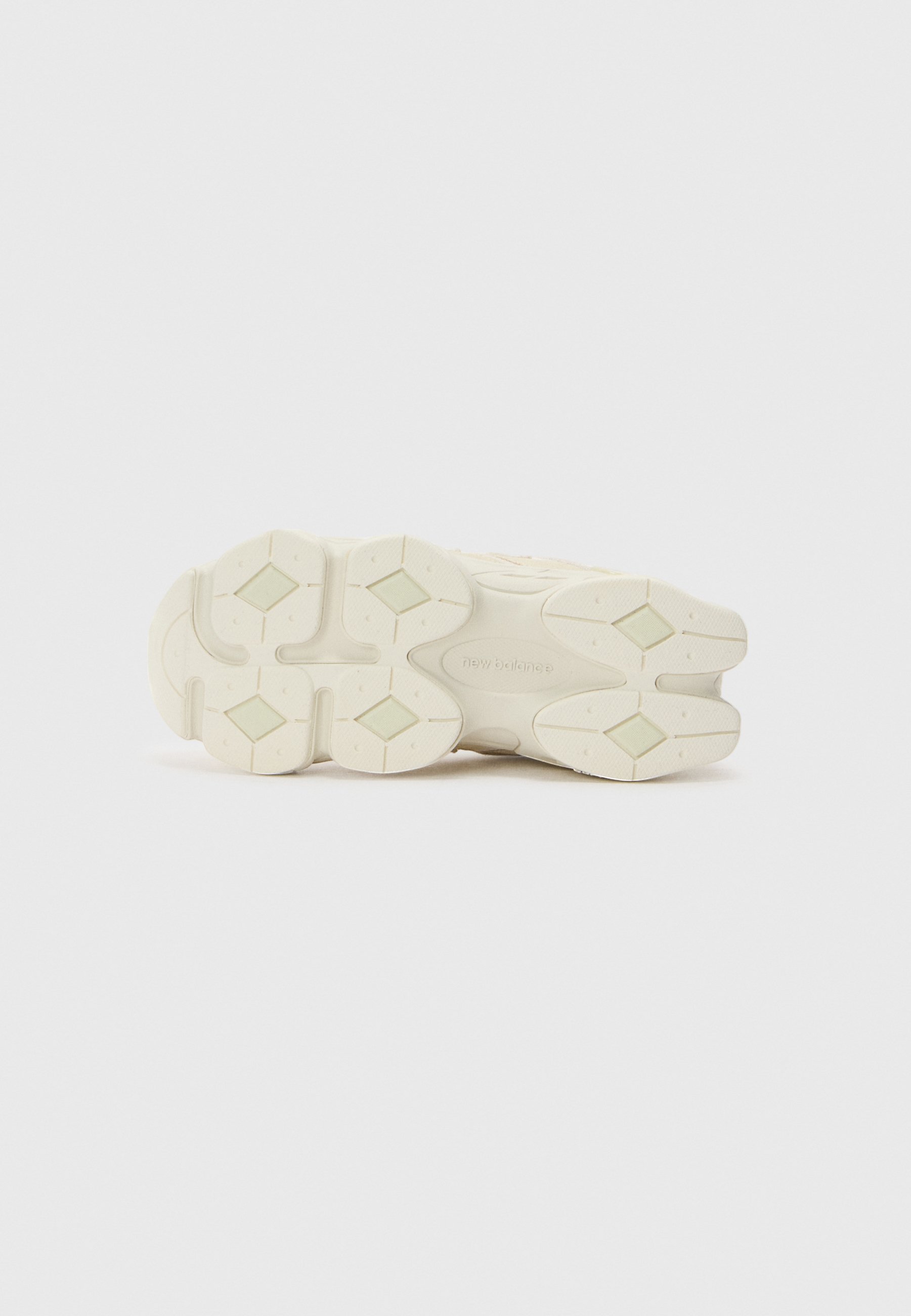 Suela de una zapatilla blanca con patrones de tracción en forma de diamante y la marca "new balance" en el centro sobre un fondo liso.