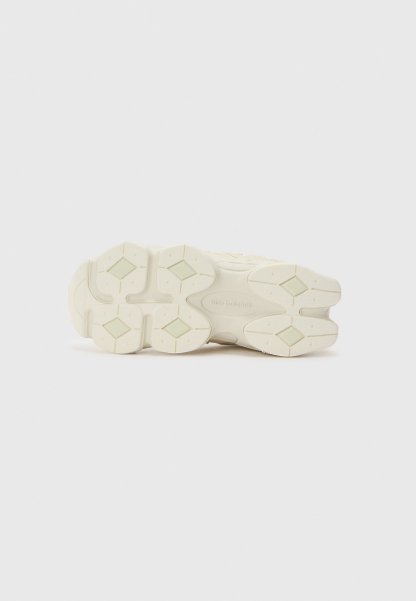 Suela de una zapatilla blanca con patrones de tracción en forma de diamante y la marca "new balance" en el centro sobre un fondo liso.