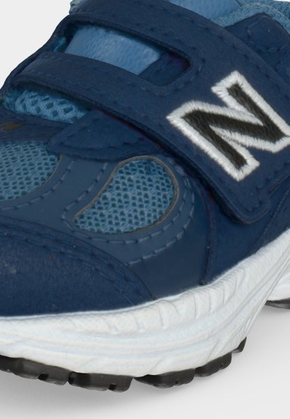 Primer plano de zapatilla azul marino con tejido de malla, tira de velcro y suela blanca con una destacada letra N cosida.