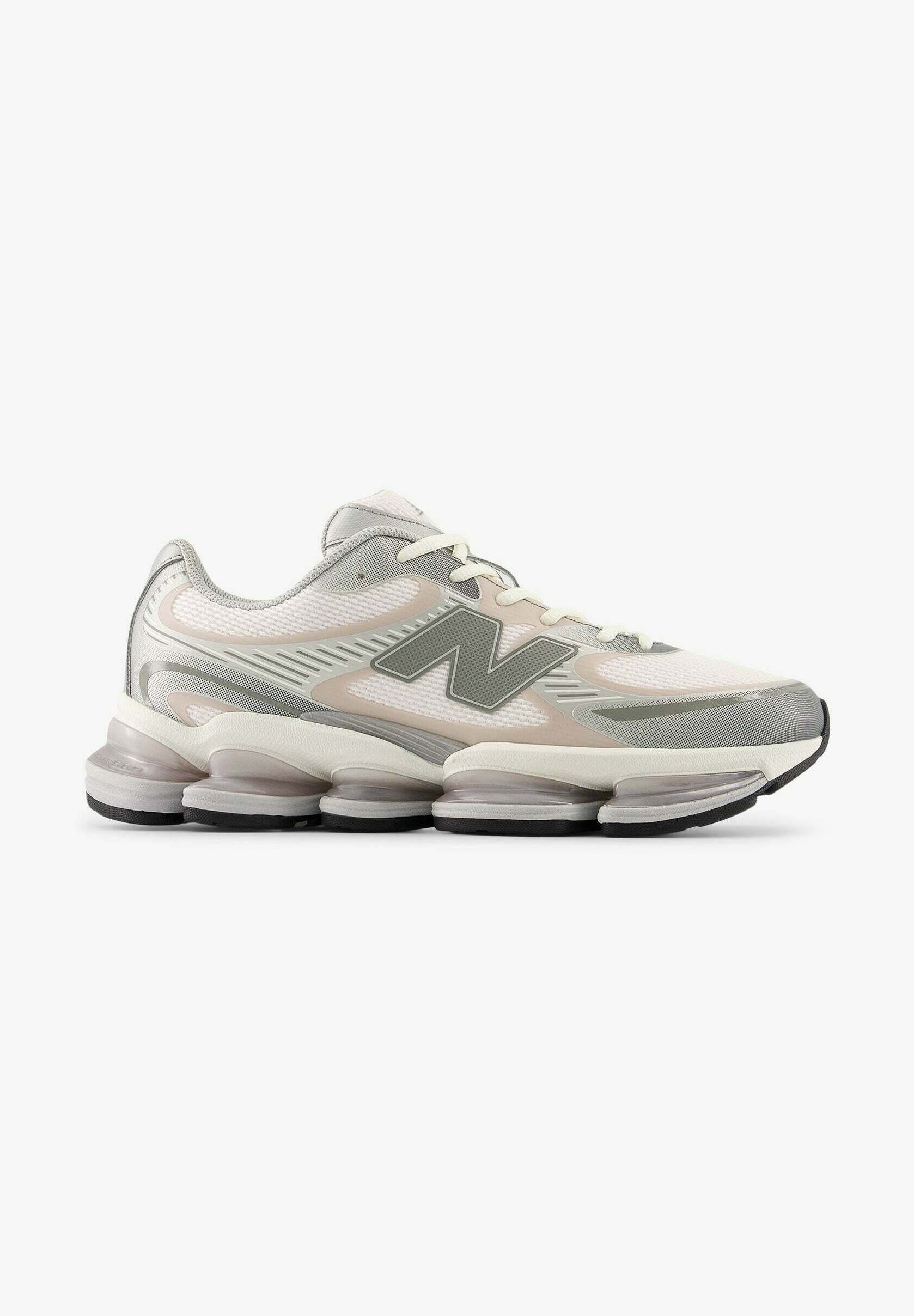 Zapatilla deportiva New Balance blanca y gris con parte superior de malla, suela acolchada con unidades de aire visibles y cierre de cordones, vista lateral.