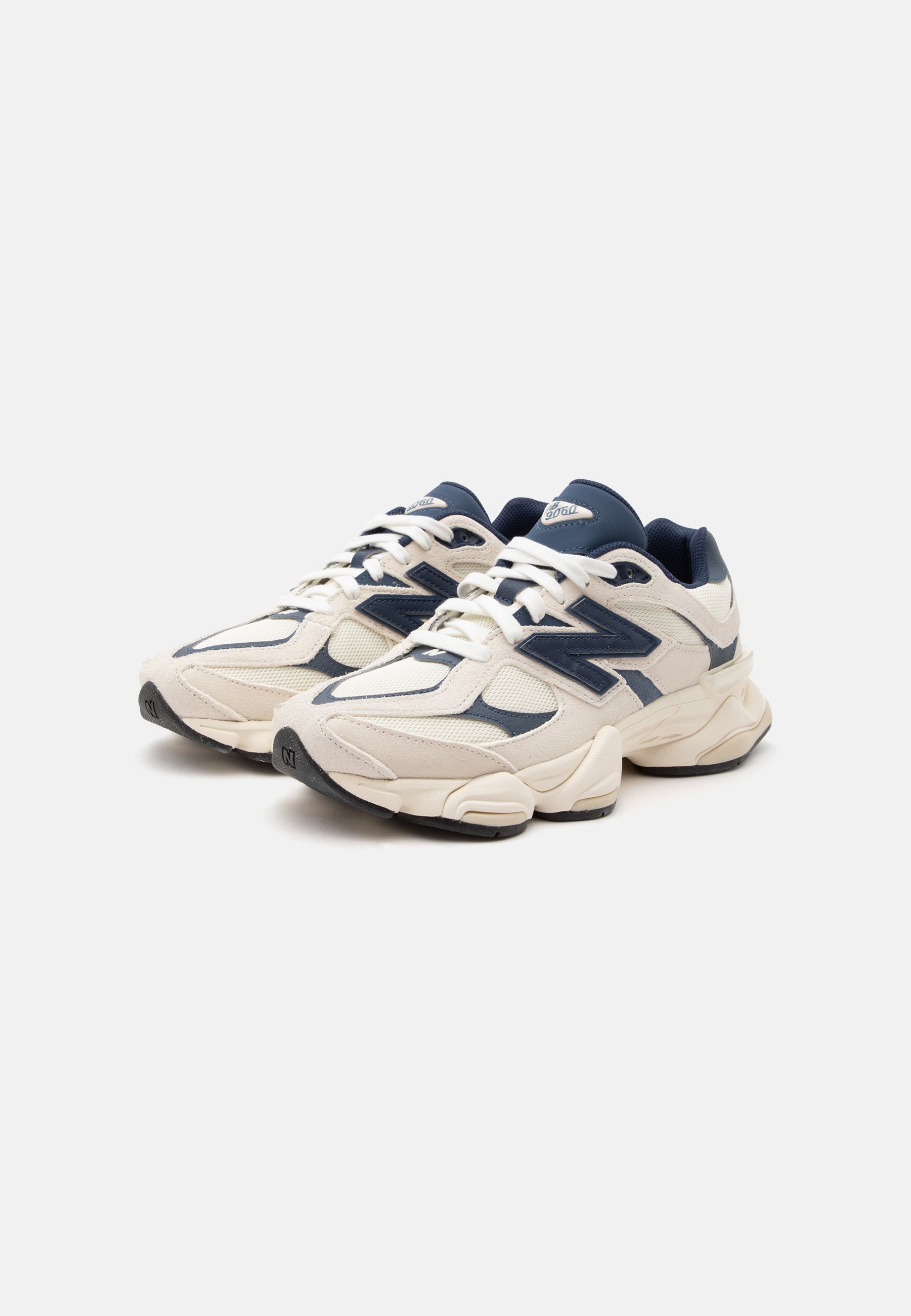 Par de zapatillas deportivas New Balance blancas y azul marino con suelas gruesas, cordones y detalles de tejido de malla sobre un fondo blanco.