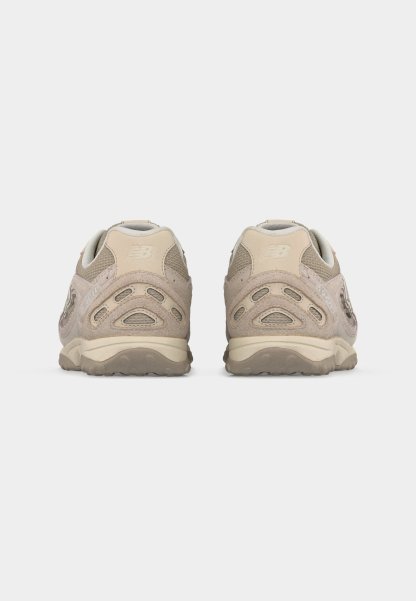 Par de zapatillas para correr New Balance en tonos beige y marrón claro, mostradas desde atrás sobre un fondo blanco.