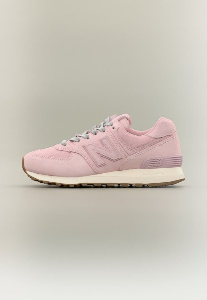 Zapatilla New Balance de color rosa claro con cordones grises, entresuela beige y suela exterior marrón, mostrada desde el lado exterior sobre un fondo neutro.