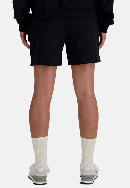 Persona con pantalones cortos negros, calcetines crema hasta la pantorrilla y zapatillas blancas New Balance, vista desde atrás sobre un fondo liso.