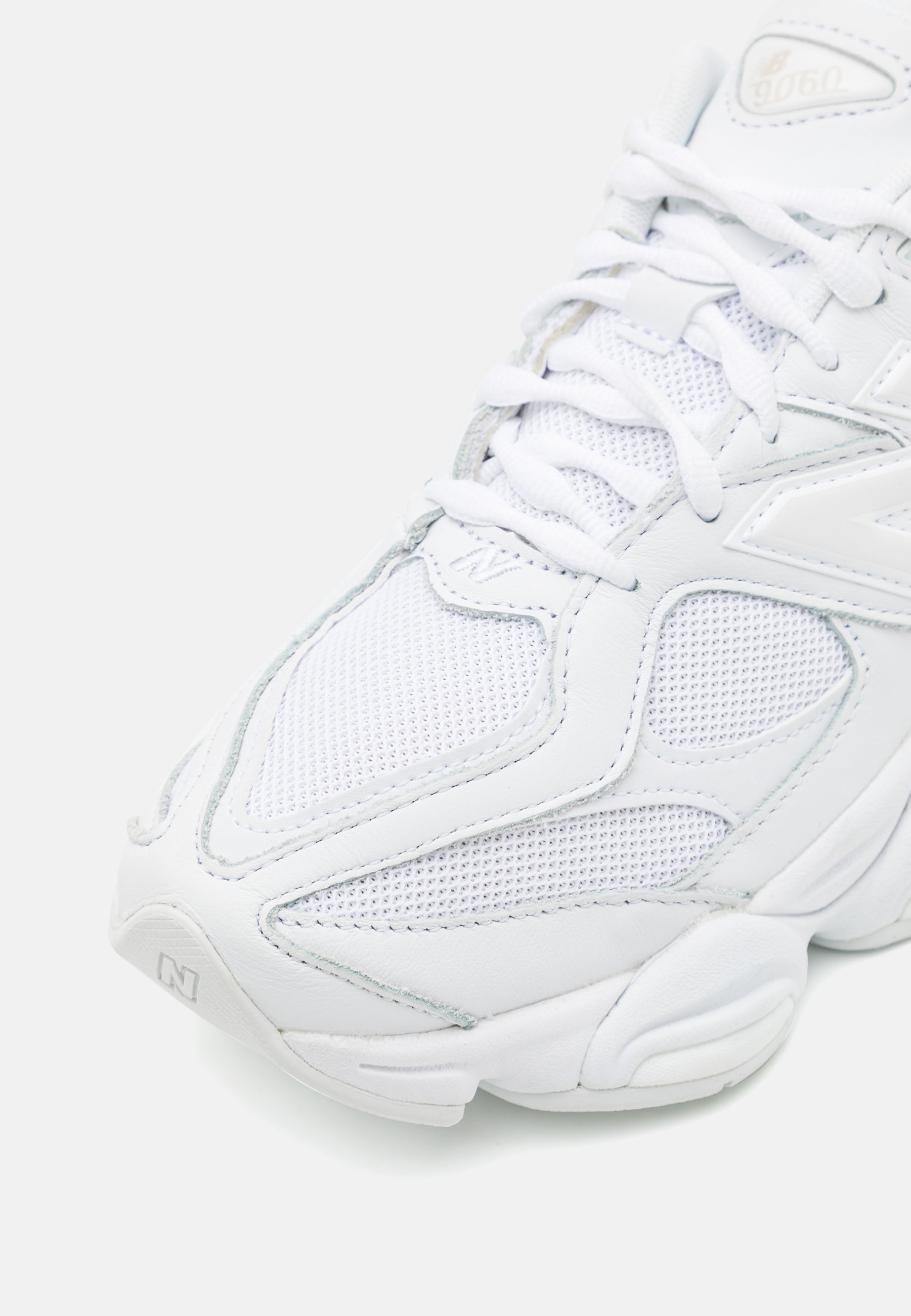 Zapatilla deportiva blanca con parte superior de malla y cuero, que presenta un acabado texturizado, lengua acolchada y una suela que ofrece soporte con un branding sutil.