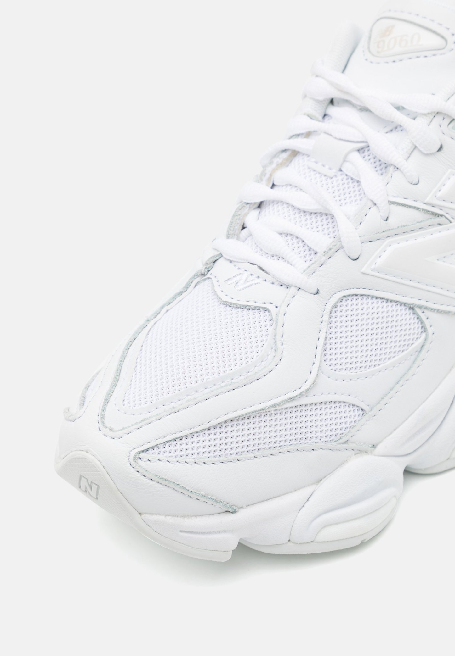 Zapatilla deportiva blanca con parte superior de malla y cuero, que presenta un acabado texturizado, lengua acolchada y una suela que ofrece soporte con un branding sutil.