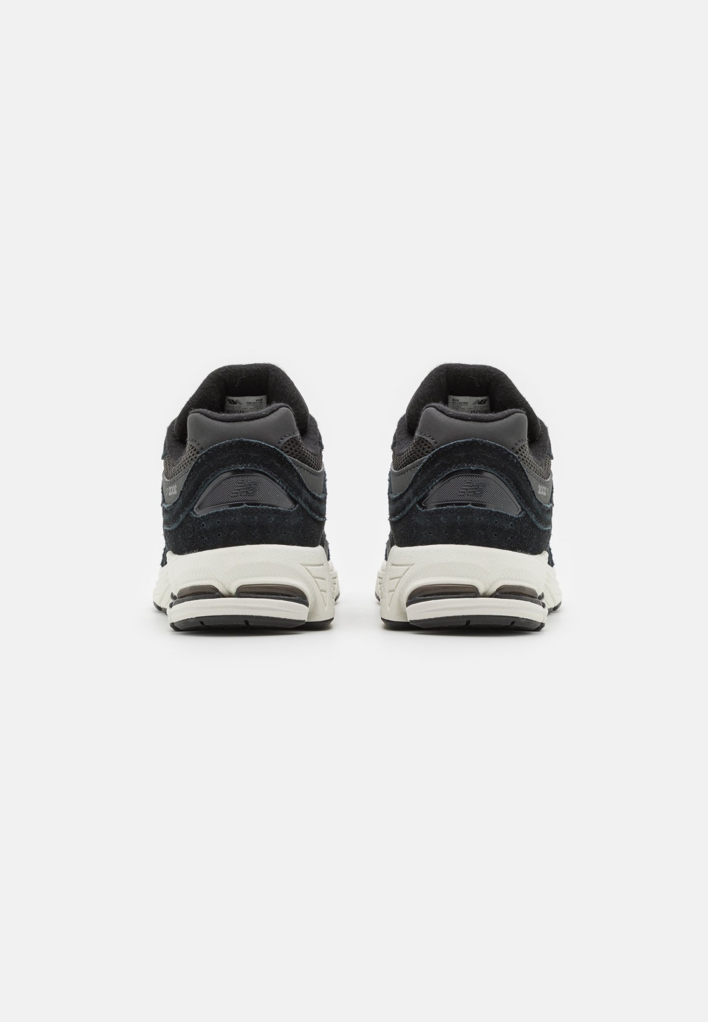 Zapatillas deportivas negras y grises con un acabado de ante texturizado, un collar acolchado y suelas de goma blancas en contraste. La vista trasera muestra detalles de amortiguación.