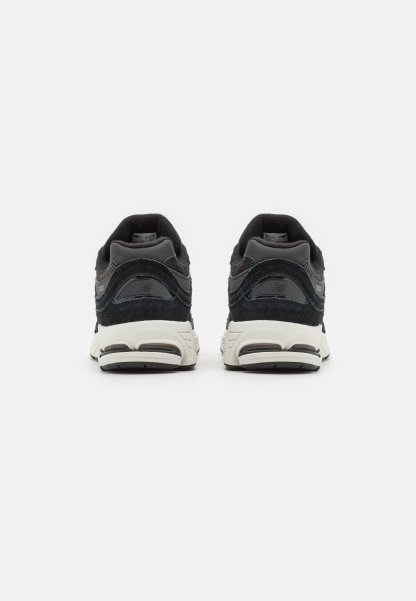 Zapatillas deportivas negras y grises con un acabado de ante texturizado, un collar acolchado y suelas de goma blancas en contraste. La vista trasera muestra detalles de amortiguación.