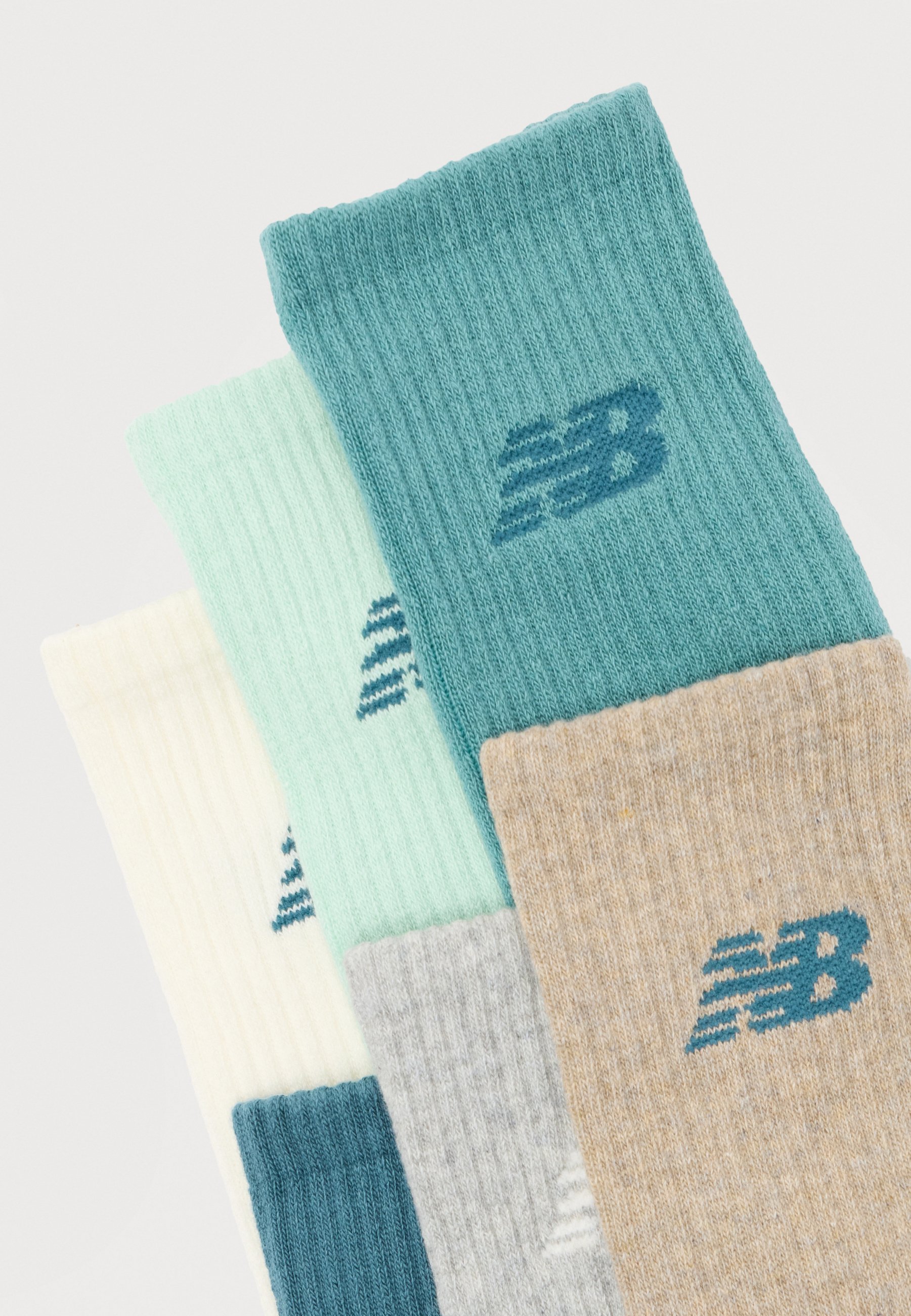 Tres pares de calcetines New Balance de caña apilados, en colores azul verdoso, beige, verde menta, gris claro y crema, con textura acanalada.