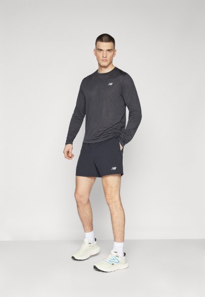 Camiseta deportiva de manga larga negra combinada con pantalones cortos azul marino, con un logo. El modelo también lleva zapatillas blancas y azules con calcetines blancos.