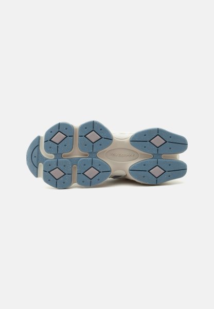 Suela de zapatilla beige New Balance con secciones de agarre de goma azul con formas de diamante y patrón de banda de rodadura texturizado.