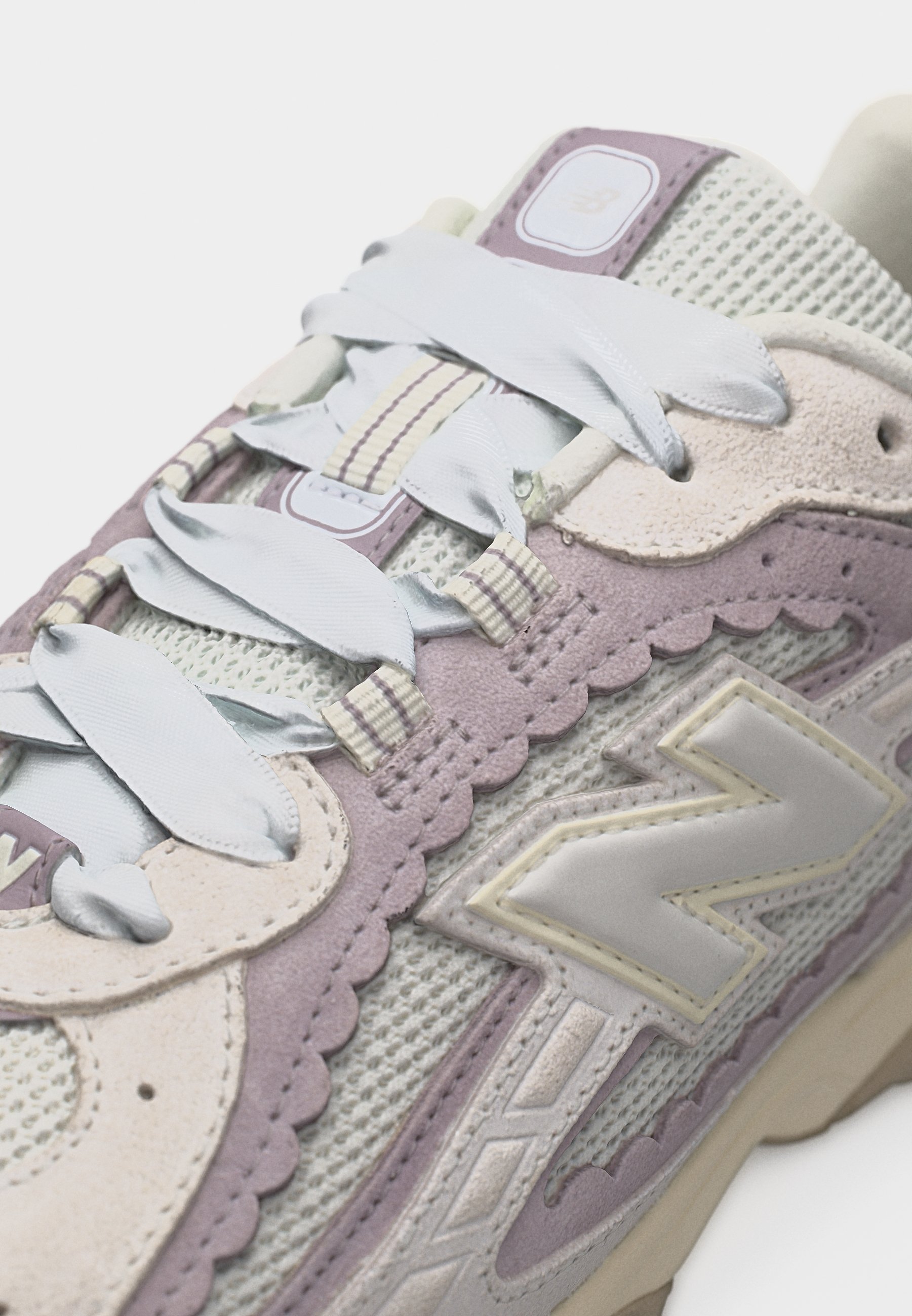 Zapatilla de malla y ante en beige y lavanda con cordones blancos y un gran logo "N" en el lateral.