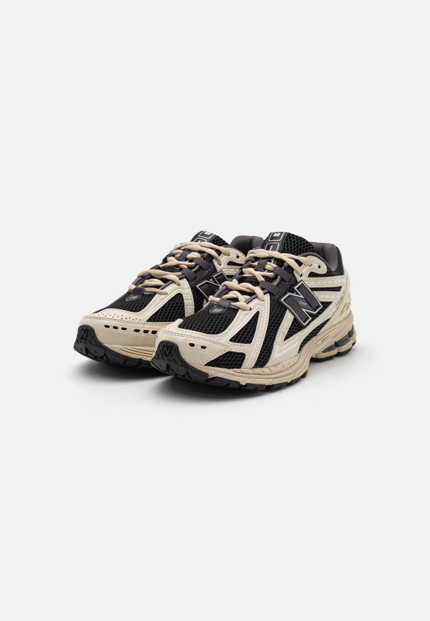 Par de zapatillas de correr New Balance negras y beige con parte superior de malla y sintética, cordones atados, mostradas desde una vista frontal en ángulo sobre fondo blanco.