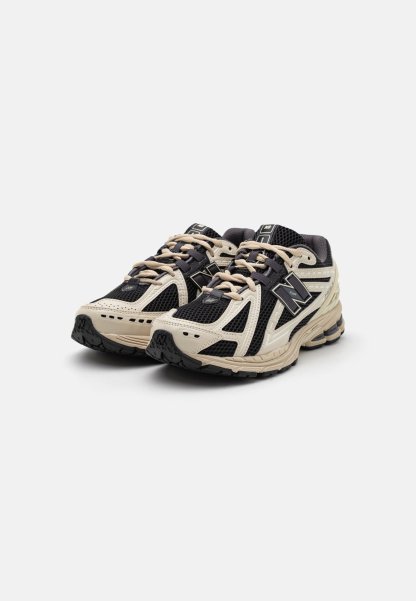 Par de zapatillas de correr New Balance negras y beige con parte superior de malla y sintética, cordones atados, mostradas desde una vista frontal en ángulo sobre fondo blanco.